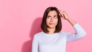 Eine junge Frau kratzt sich am Kopf und schaut dabei fragend in die Ecke. Die Mimik deutet an, dass sie etwas vergessen hat. 