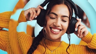 Eine junge Frau hört Musik mit Kopfhörern und lächelt dabei.
