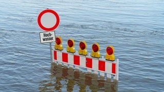Eine Straßenabsperrung ist vom Hochwasser des Rheins überflutet.