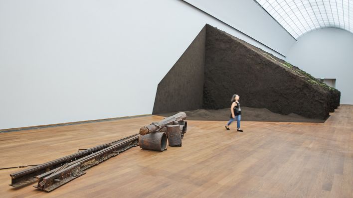 Eine Frau läuft am 08.07.2025 bei einer Vorbesichtigung an dem Kunstwerk von Delcy Morelos im Hamburger Bahnhof vorbei - im Vordergrund ist ein Kunstwerk von Joseph Beuys zu sehen (Quelle: imago images/Funke Foto Services)