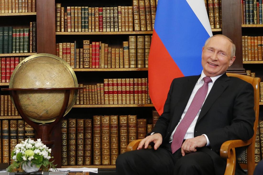 Wladimir Putin sitzt in einem Stuhl und lacht. 