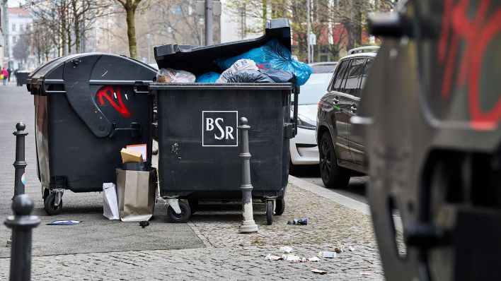 Symbolbild: Überfüllte Mülltonnen mit offenem Deckel und herumliegendem Abfall auf Gehweg in Berlin, städtische Müllentsorgung in einer Wohngegend. (Quelle: dpa/Bihlmayer)