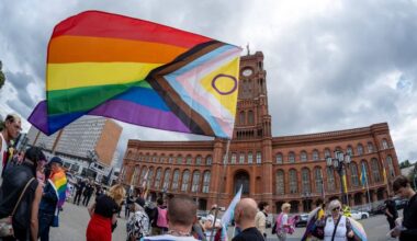 Demonstranten gegen queerfeindliche Hetze schwingen vor dem Roten Rathaus in Berlin eine inklusive Regenbogenflagge. (Quelle: imago-images/Seeliger)