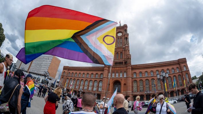 Demonstranten gegen queerfeindliche Hetze schwingen vor dem Roten Rathaus in Berlin eine inklusive Regenbogenflagge. (Quelle: imago-images/Seeliger)