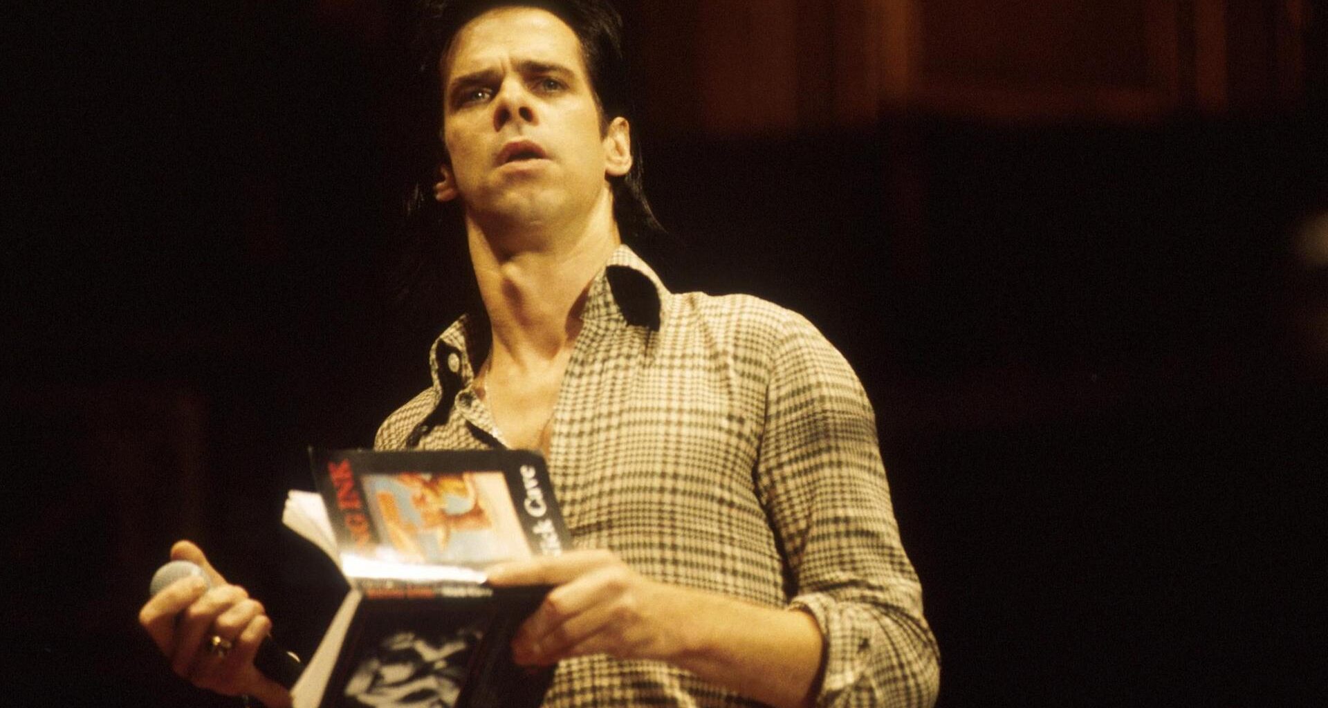 Porträt von Nick Cave, der ein Buch in der Hand hält.