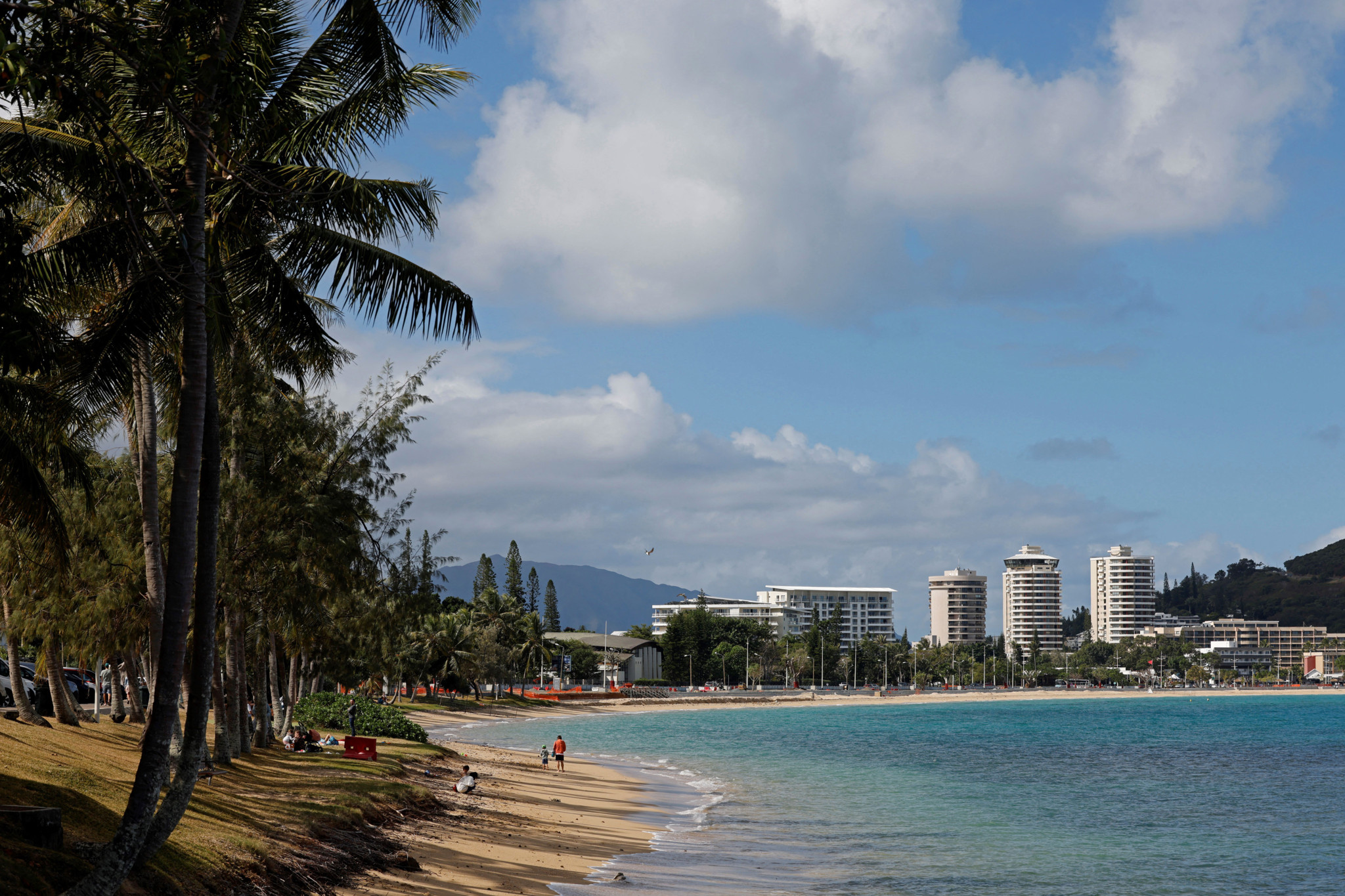 Strand von Noumea mit Spaziergängern, Palmen und Hochhäusern im Hintergrund, aufgenommen am 23. Juli 2023.