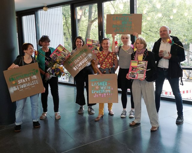 Mit Blumensträußen, Pflasterstein und besprühten Pappschildern setzen sich Bürger*innen im Rathaus Kreuzberg für die Erweiterung der Laskerwiese ein.