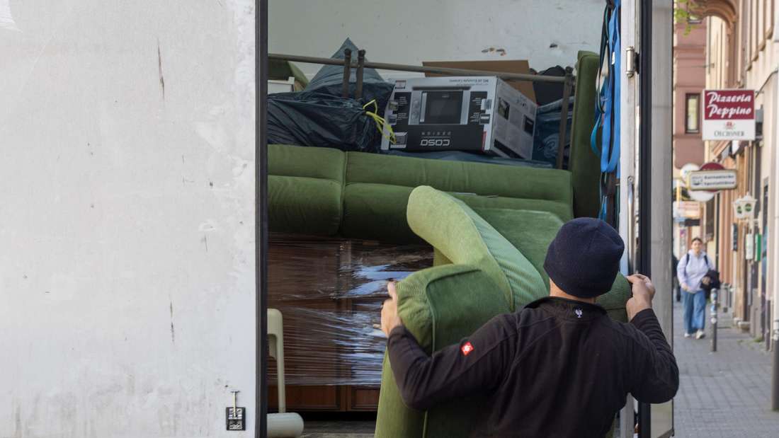 Ein Möbelpacker schleppt einen grünen Sessel in einen Umzugswagen.