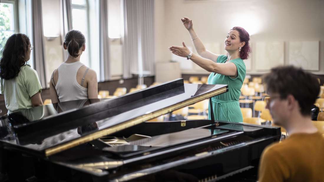 Wiesbaden, 30.06.2025u000dfür TdT Quereinsteigerinnen in den Lehrerberuf, Stimmbildnerin Marina Russmann, Oranienschule, Wiesbaden, im Bild: Probe Oberstufenchor in der Aula u000dfür Auftritt Kulturnacht mitu000du000dStimmbildnerin Marina Russmannu000d(Opern- und Konzertsängerin und Gesangspädagpgin)u000dim Referendariat zur Musiklehrerin, u000dChorleiter Tobias Hahn (r.) am Flügelu000dFoto: Michael Schick, Bertramstr. 19, 65185 Wiesbaden, Tagespauschale