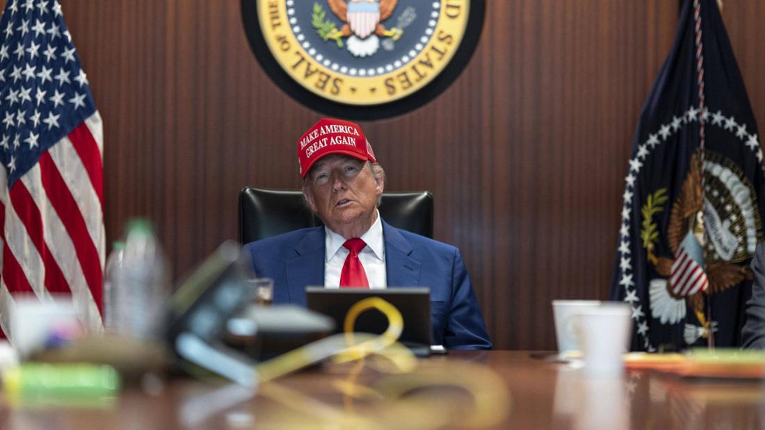 Donald Trump sitzt mit Cap an einem Tisch