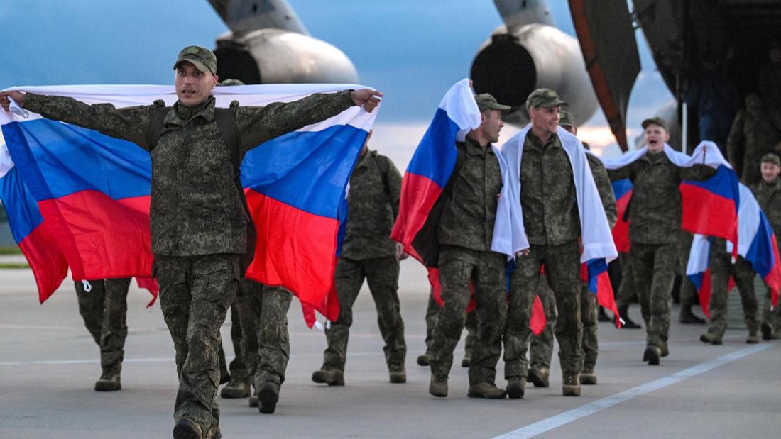 Soldaten mit russischen Flaggen gehen vor Flugzeug über Asphalt