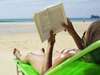 Eine Frau liest ein Buch am Strand (Symbolbild)