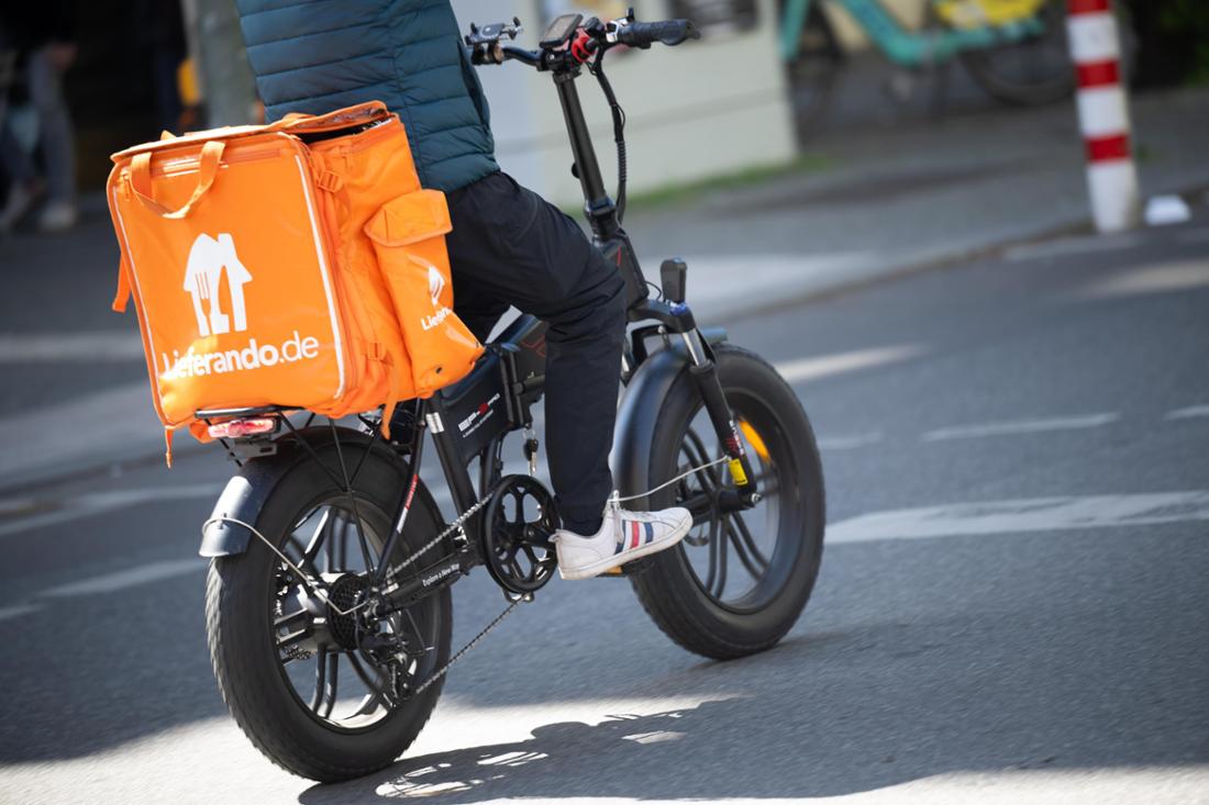 Ein Fahrer für den Essenslieferdienst Lieferando fährt mit einem Rad über eine Straße.