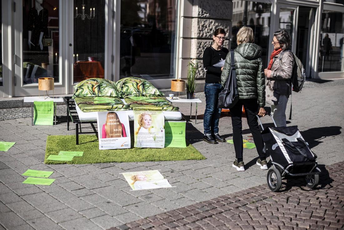 Auf dem Schlossplatz in Wiesbaden steht ein Ehebett, darauf Bettdecken und Kissen mit grünem Muster. Damit will der Verein Wildwasser auf das Projekt „Medizinische Soforthilfe nach Vergewaltigung“ aufmerksam machen. 