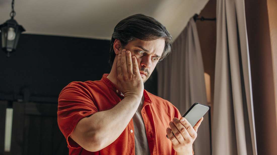 Mann guckt schockiert auf sein Handy.
