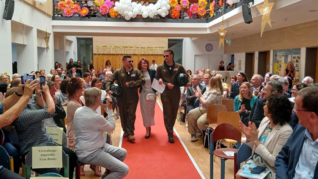 Wird von zwei als Piloten verkleideten Herren zu ihrem Platz vor der Bühne in der Kerschensteiner Grund- und Mittelschule geleitet: Claudia Frisch.  