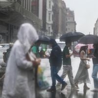 Regen in Berlin: Passantinnen und Passanten laufen in Regenjacken und mit Schirmen durch Berlin