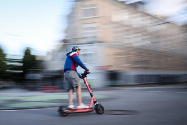 Ein Mann fährt auf einem E-Scooter. Das Bild ist leicht verwischt und soll Geschwindigkeit suggerieren.