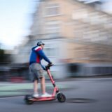 Ein Mann fährt auf einem E-Scooter. Das Bild ist leicht verwischt und soll Geschwindigkeit suggerieren.