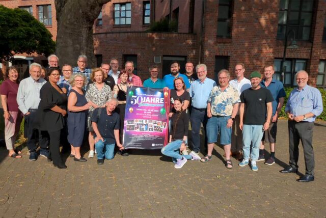 Ein Teil der Akteurinnen und Akteure der Jubiläumsrevue zum 50. Geburtstag der „Städteehe“ zwischen Herten und Westerholt / Bertlich präsentieren das Plakat zum Event am 30. August um 19 Uhr auf der Zeche Schlägel & Eisen.