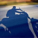 Der Schatten eines Motorradfahrers ist auf einer Straße zu sehen. Die Aufnahme wurde mit Bewegungsunschärfe erzeugt, was auf eine hohe Geschwindigkeit hindeutet.