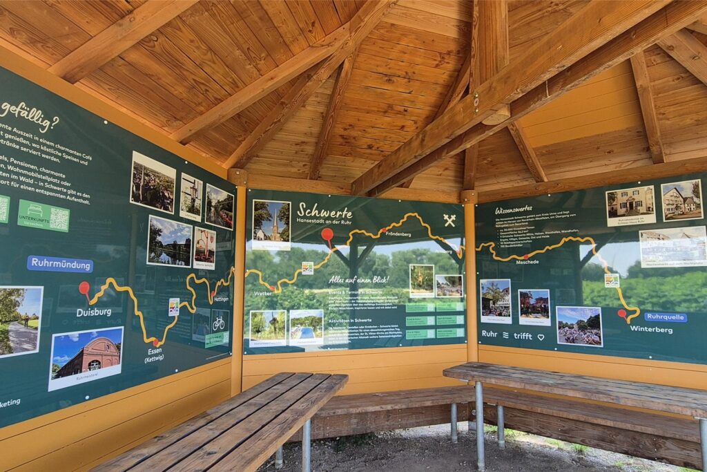 Blick in die hölzerne Rasthütte am Ruhrtalradweg in Schwerte. An den Wänden hängen Infotafeln, die über Schwerte informieren. 