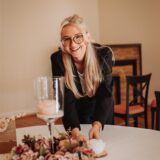 Hochzeitsplanerin Michelle Potrafke lehnt sich an einen Tisch und lächelt.