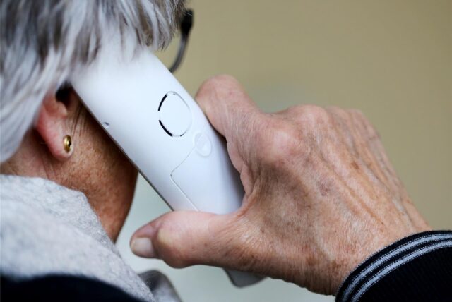Man sieht eine Seniorin mit einem Festnetztelefon (von hinten aufgenommen)