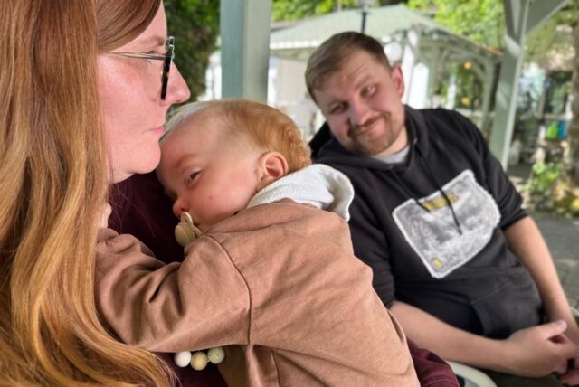 Toni auf dem Arm seiner Mutter Johanna. Im Hintergrund ist Papa Patrick zu sehen.