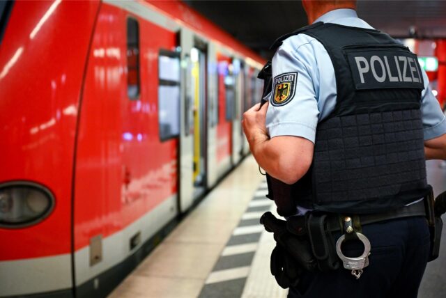 Ein Beamter der Bundespolizei steht an einer Plattform eines Bahnhofes neben einem haltenden roten Zug.