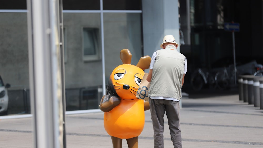 Ein Mann fotografiert die durch ein Feuer an der Seite beschädigte Maus vor dem WDR-Gebäude.