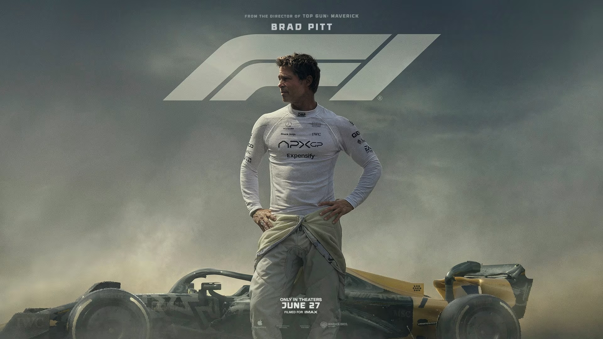 Ein Rennfahrer steht vor einem Formel-1-Auto in einem Rennanzug mit den Händen in die Hüften gestützt. Im Hintergrund ist das F1-Logo sichtbar.