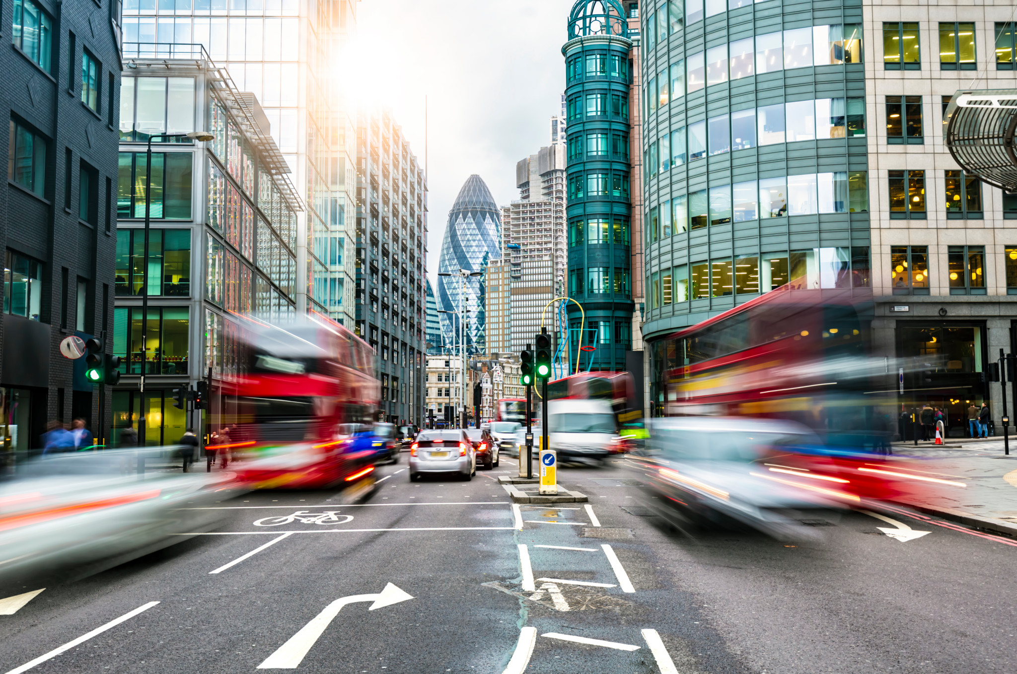 Belebte Strasse in London mit mehreren roten Doppeldeckerbussen und modernen Hochhäusern im Hintergrund.