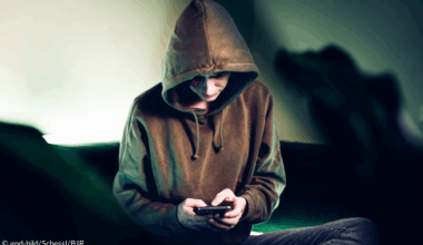Junge mit Kapuzenpullover und Handy in der Hand