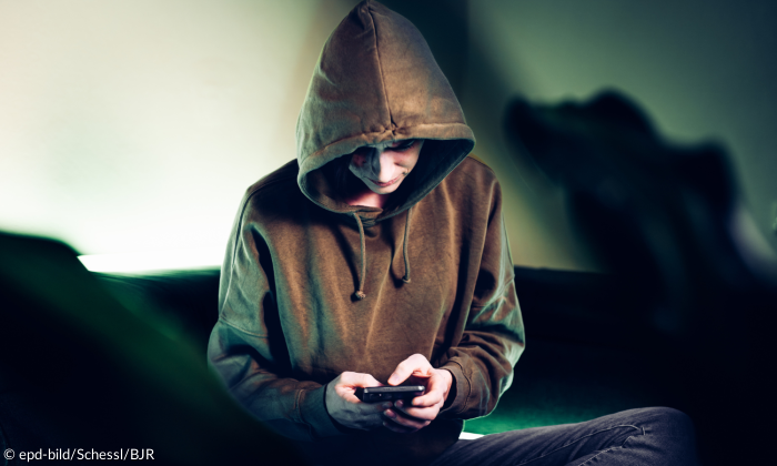 Junge mit Kapuzenpullover und Handy in der Hand