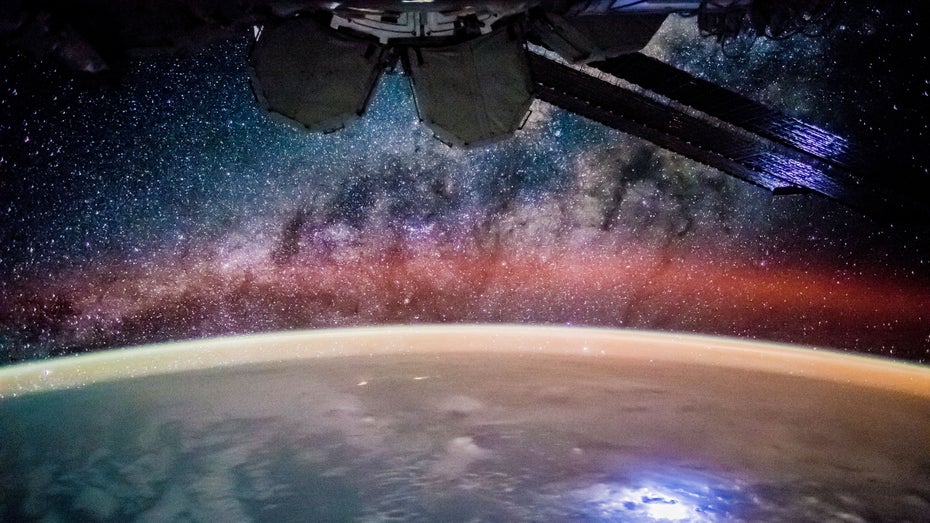 Die ISS schwebt über der Erde und durch einen sternenbesetzten Himmel.