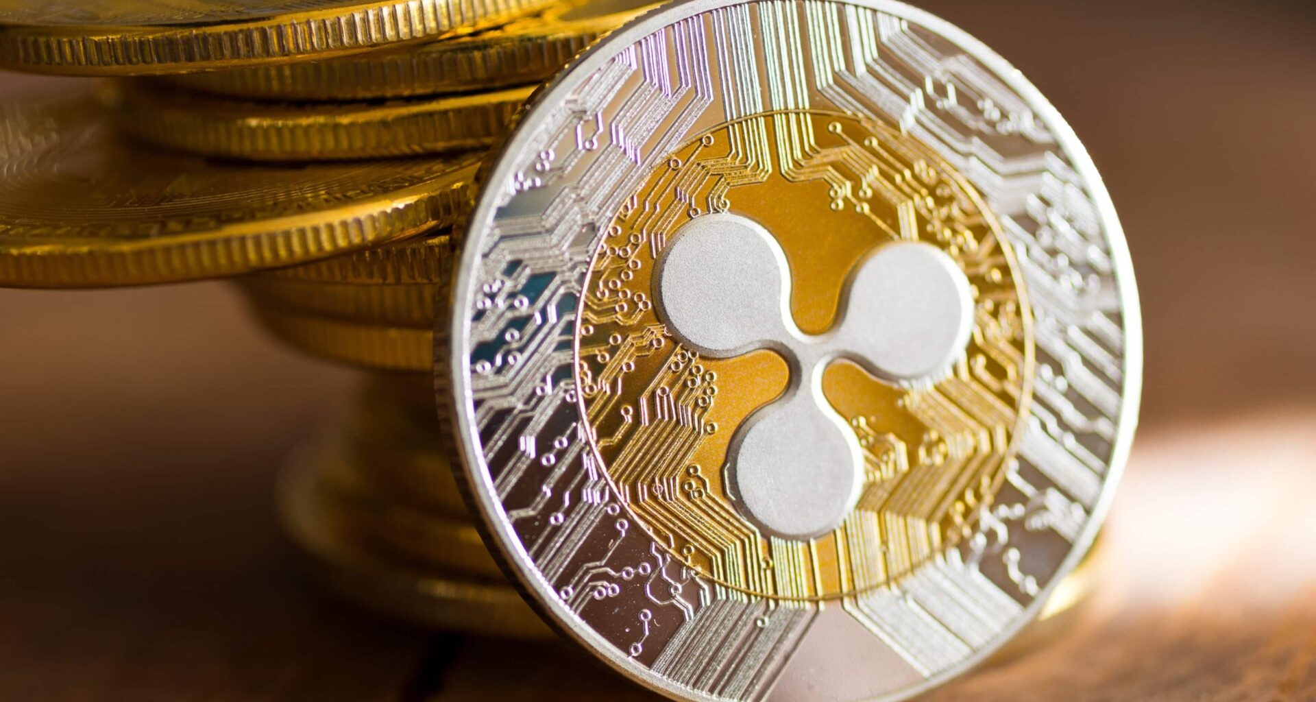 Eine Nahaufnahme einer XRP-Kryptowährungsmünze mit ihrem Logo, mit einem Stapel ähnlicher XRP-Münzen im Hintergrund auf einer Holzoberfläche.