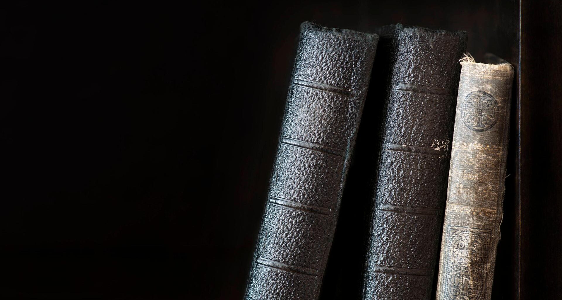 Drei alte, historische Bücher stehen aneinander gelehnt in einem Regal
