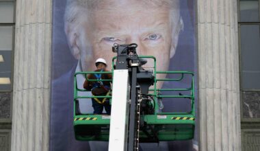 Donald Trump als Plakat. Seine Augen sind hinter einer Plattform zu erkennen, auf der ein Arbeiter steht. Vermutlich bringt dieser gerade das überlebensgroße Banner an