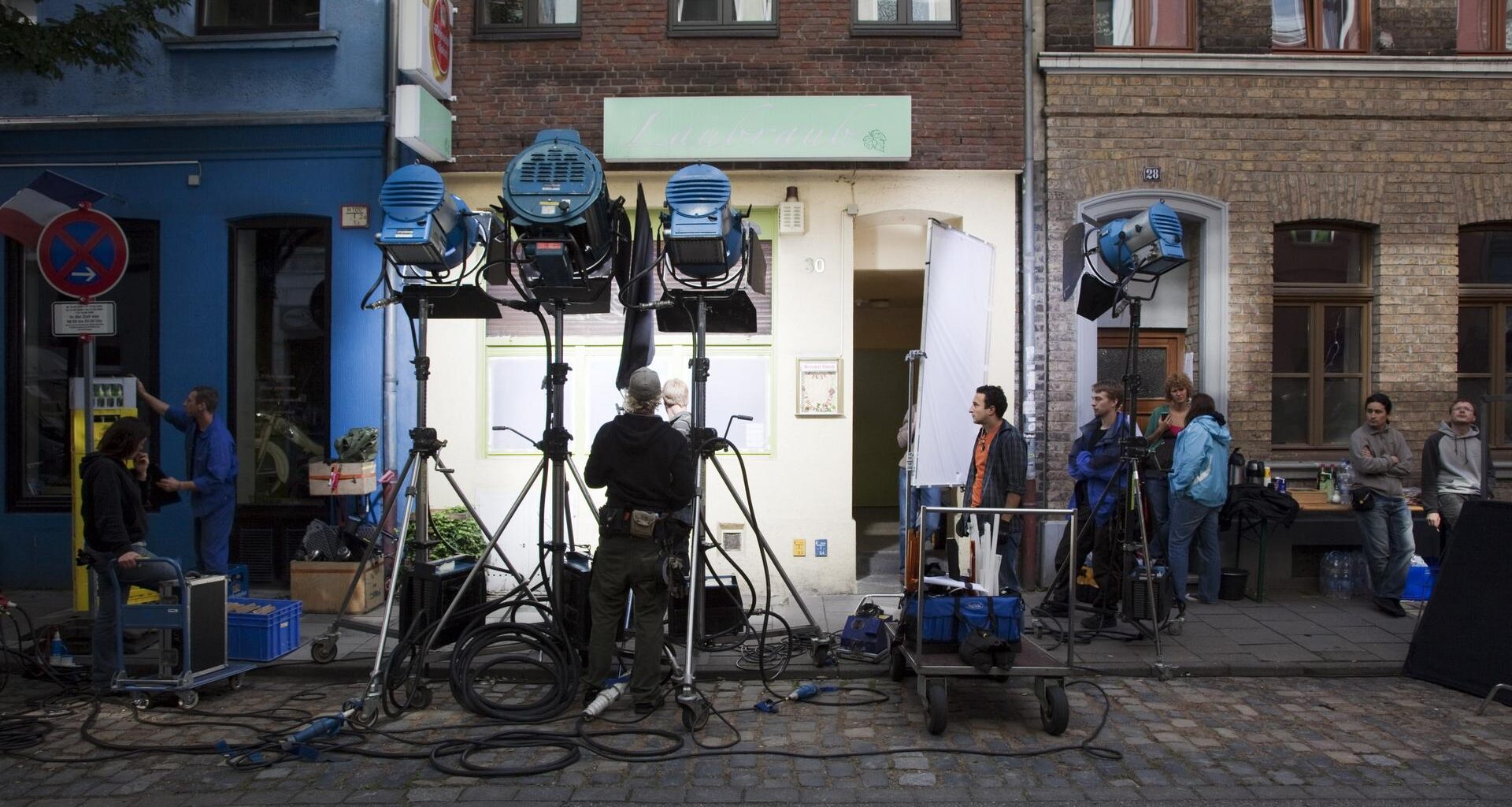 Eine Filmcrew baut ein Set mit Scheinwerfern vor einem Mehrfamilienhaus auf