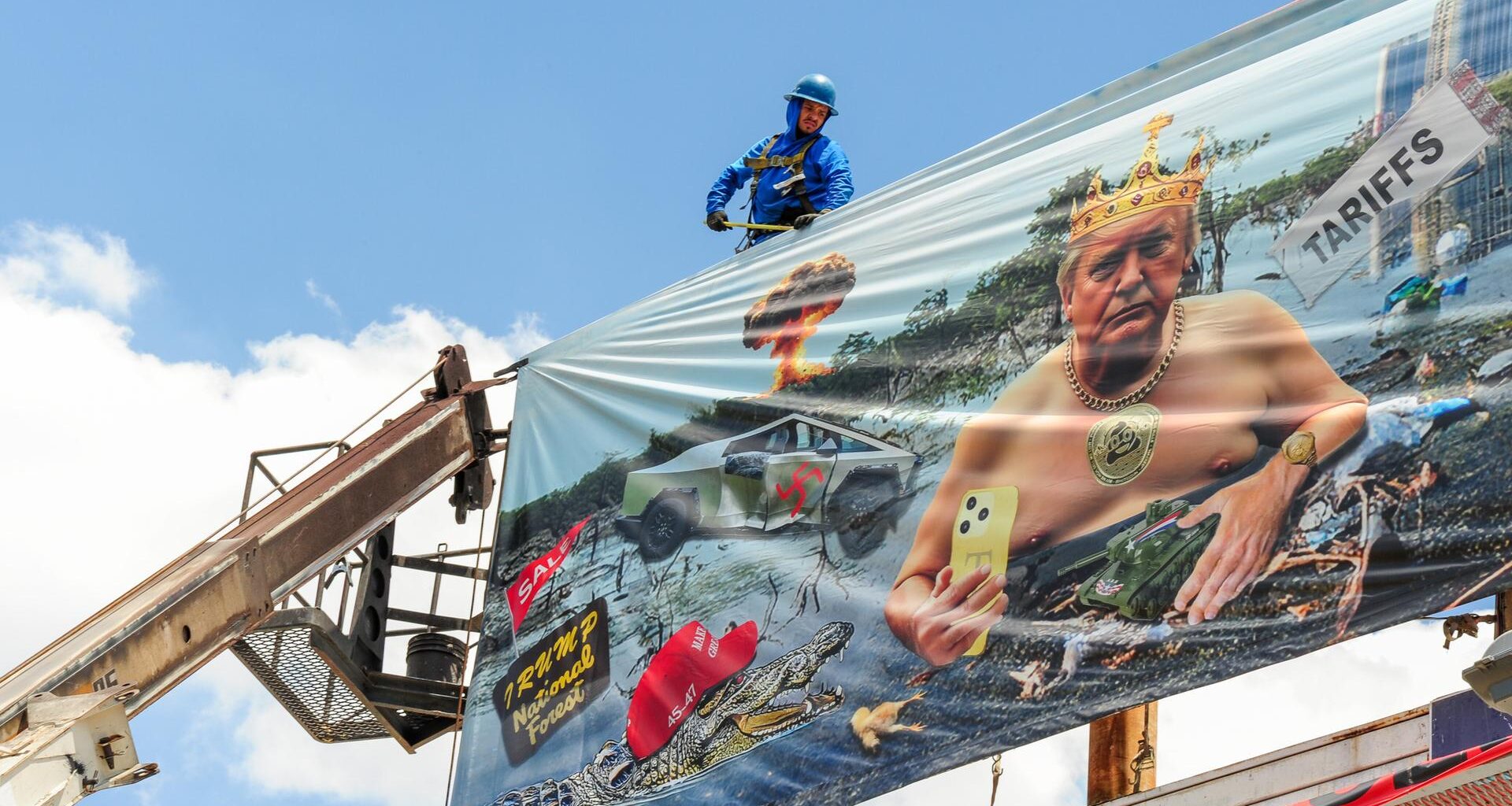 Arbeiter installieren eine Plakatwand der Künstlerin Karen Fiorito in Phoenix. Das Werk mit dem Titel „Swamp King“ kritisiert Donald Trumps Präsidentschaft mit Bildern, die Korruption, Autoritarismus und systemischen Verfall symbolisieren.