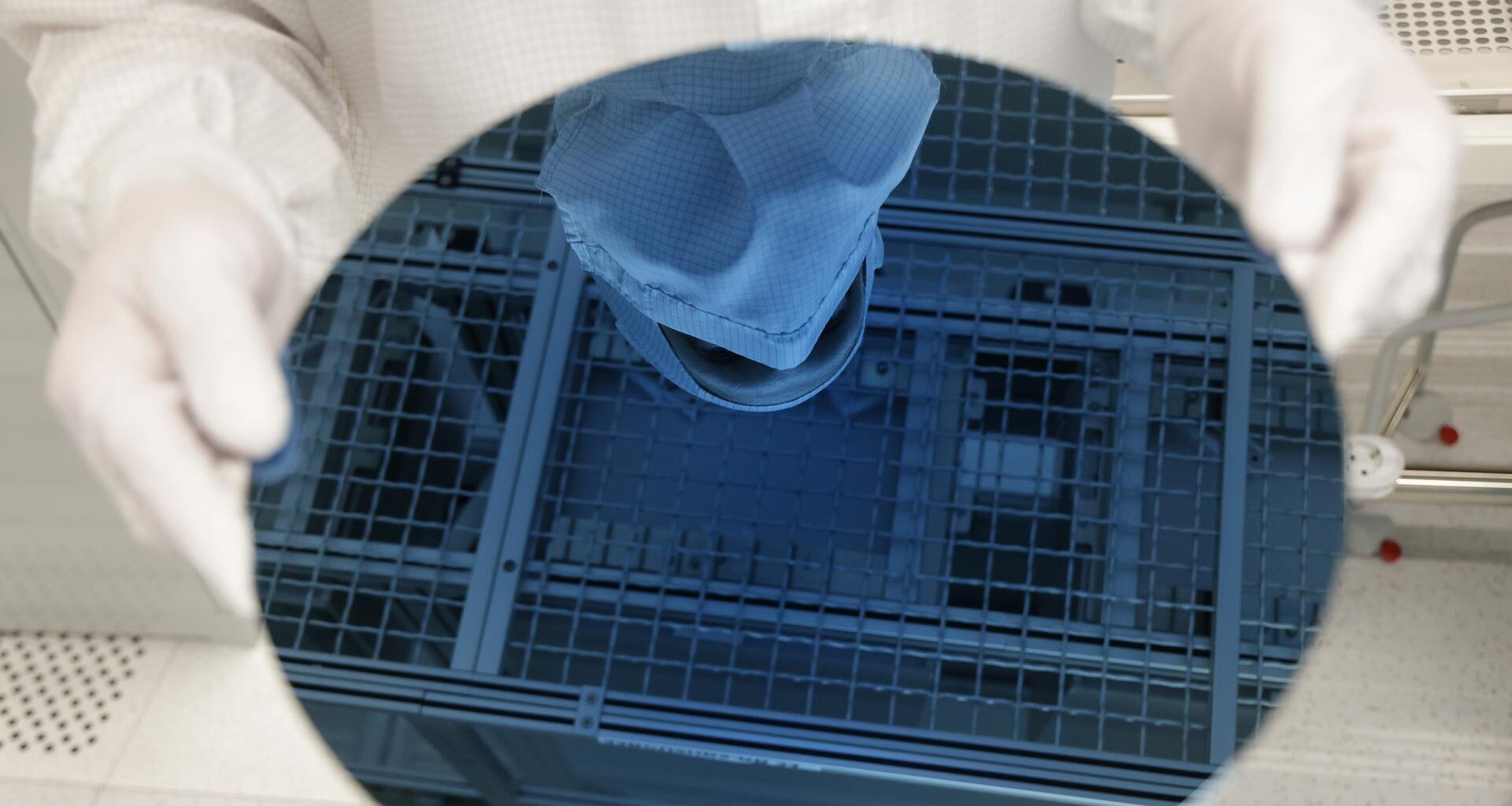 Ein Mitarbeiter in weißer Schutzkleidung hält einen Wafer in den Händen, eine runde, bläuliche Glasscheibe.