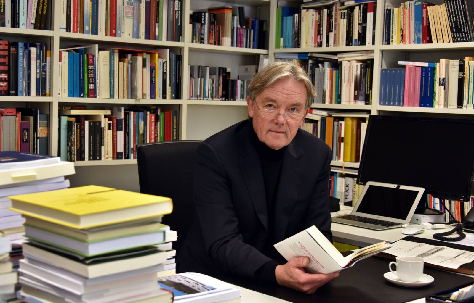 Portraitfotografie eines Mannes inmitten seiner Bücher am Schreibtisch.