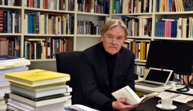 Portraitfotografie eines Mannes inmitten seiner Bücher am Schreibtisch.