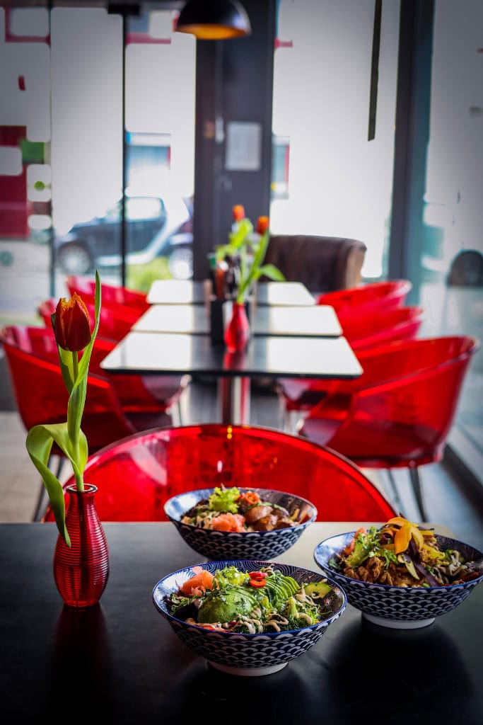 Drei bunte Bowls mit Gemüse auf schwarzem Tisch im Restaurant mit roten Stühlen und Tulpenvasen.