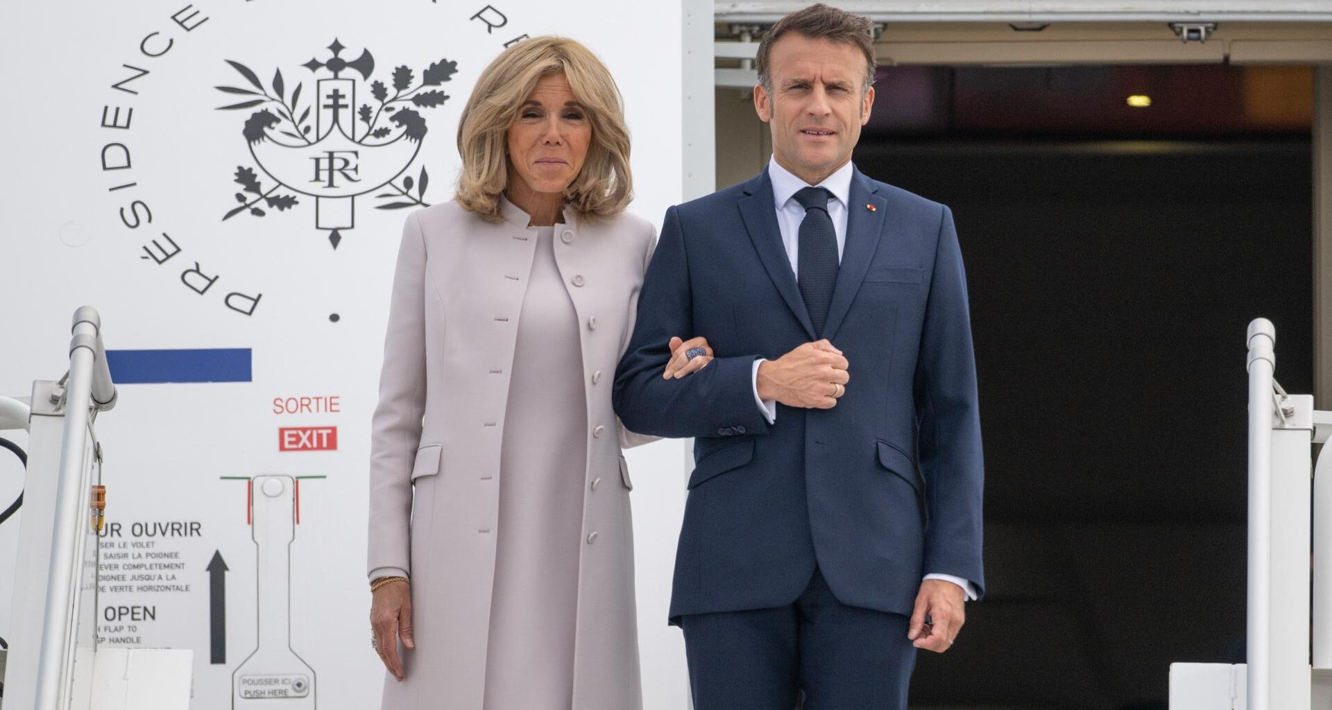 Frankreichs Präsident Macron steht gemeinsam mit seiner Frau vor der Tür eines Flugzeugs.
