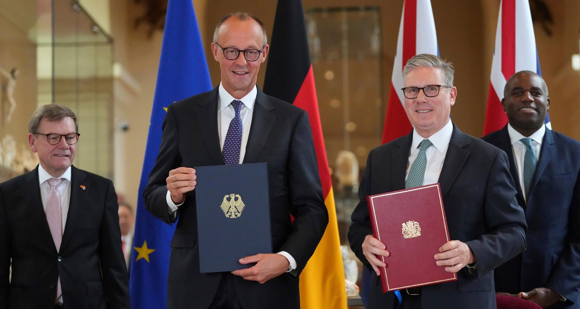 Bundeskanzler Friedrich Merz und Großbritanniens Premier Keir Starmer lächlen in die Kamera. In der Hand halten beide jeweils eine Mappe mit dem so eben unterzeichneten deutsch-britischen Freundschaftsvertrag.