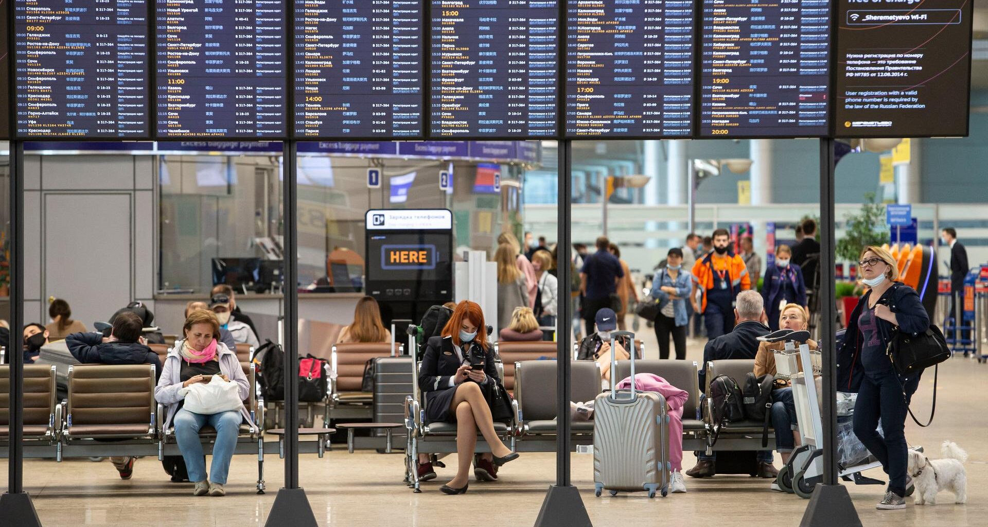 Passagiere sitzen auf dem internationalen Flughafen Scheremetjewo unter einer Fluginformationstafel.