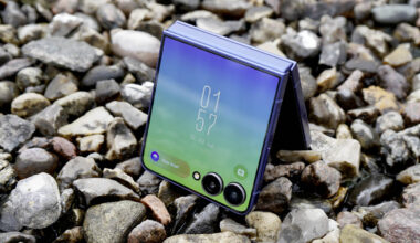 Das Samsung Galaxy Z Flip7 steht halb aufgeklappt mit eingeschaltetem Außendisplay auf einer Kiesoberfläche.