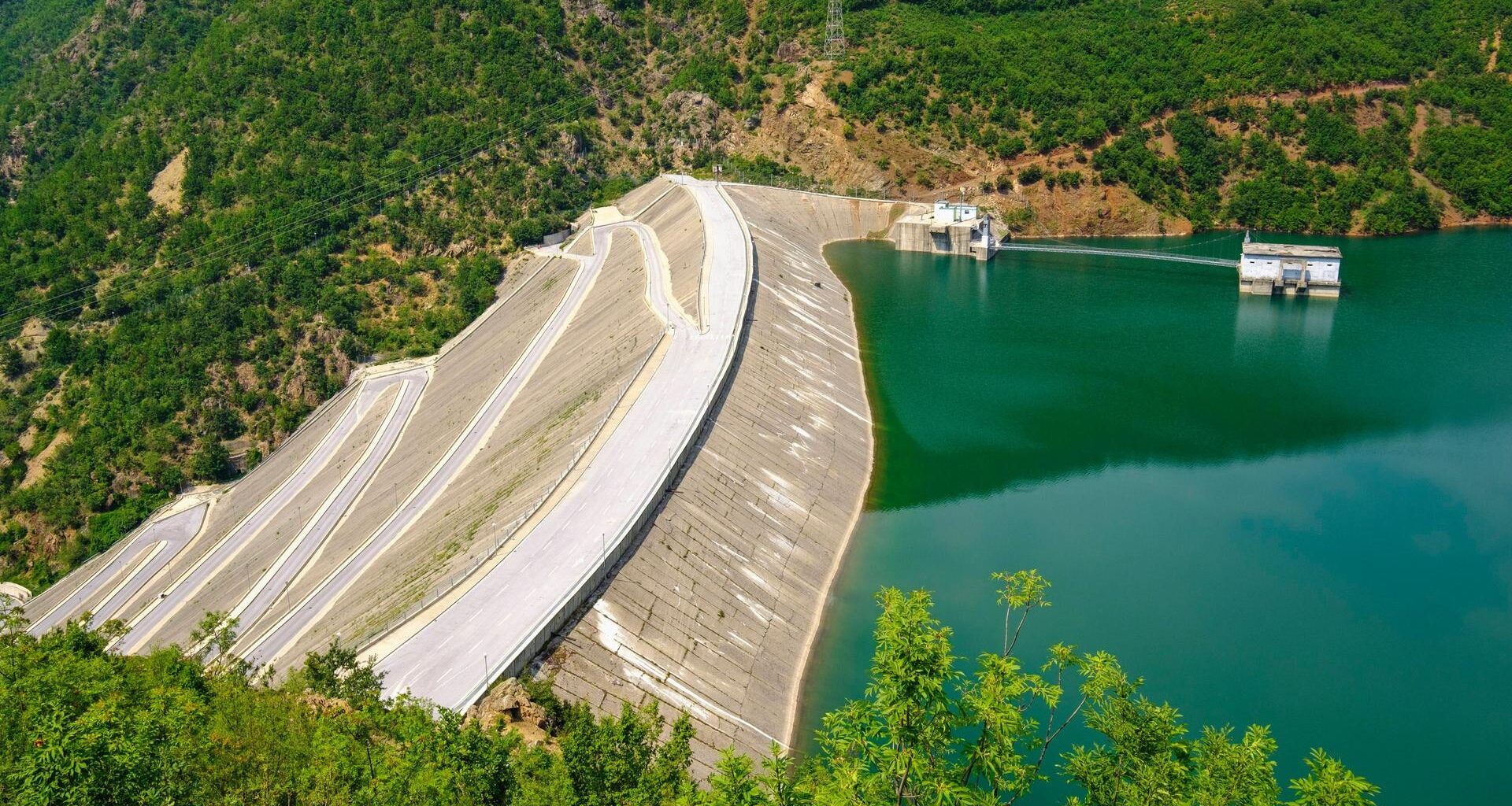 Der Fierza-Stausee ist mit seiner Fläche von 72,6 Quadratkilometern der größte Stausee in Albanien. Grünblaues Wasser wird von einer Staumauer gehalten, die weit in die Tiefe ragt.